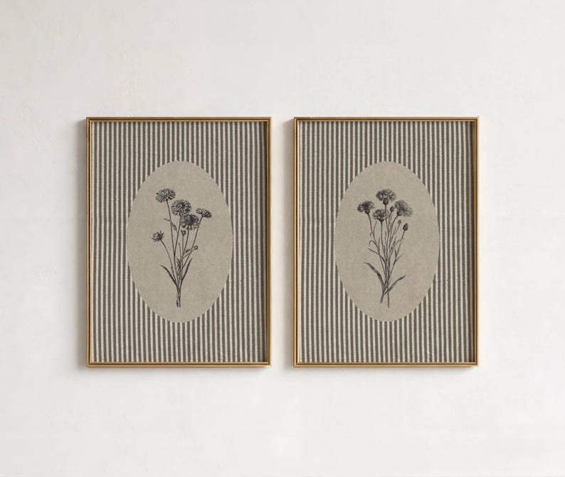 May include: Two rectangular wall art prints in thin gold frames. Each print features a vertical dark gray and white pinstripe background with a central beige oval containing a detailed black ink botanical illustration of a small flower bouquet.