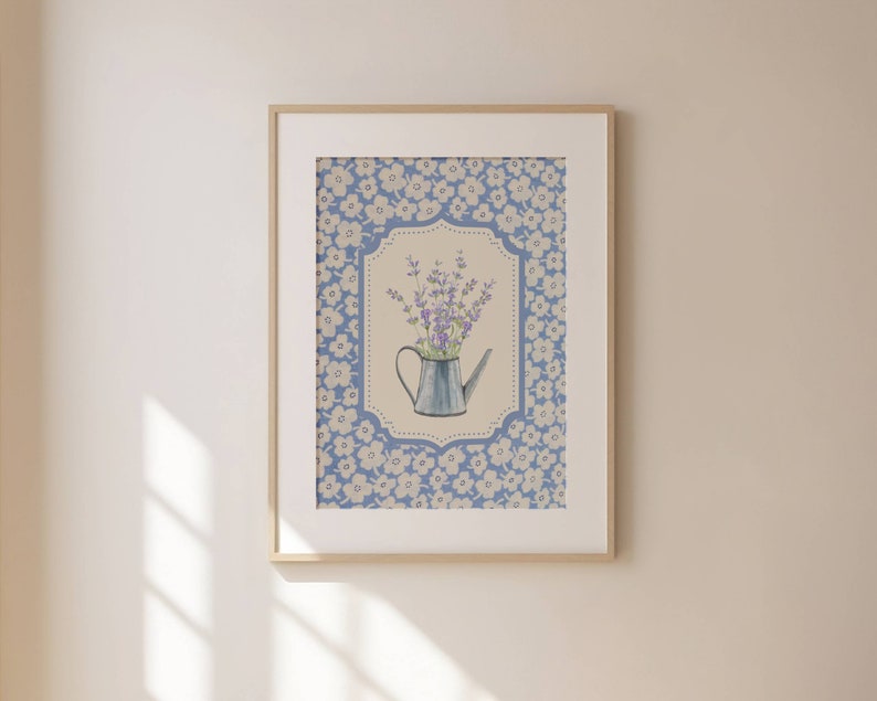 May include: Framed art print featuring a watercolor illustration of lavender in a blue watering can. The artwork is set against a floral patterned background in shades of blue and white, framed in a light wood.