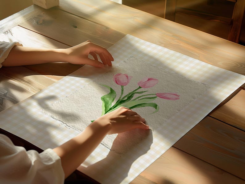 Pode incluir: Uma pe&ccedil;a retangular de papel texturizado branco sujo com uma pintura em aquarela de tr&ecirc;s tulipas cor-de-rosa com caules e folhas verdes. A obra est&aacute; centrada numa superf&iacute;cie aos quadrados bege claro e branco com sombras de luz solar.