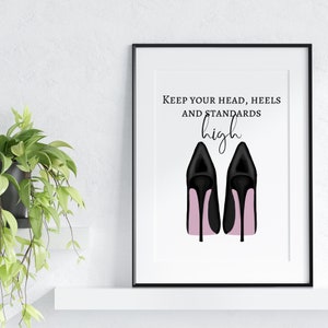 May include: A framed print featuring a pair of black high-heeled shoes with pink soles. The text "Keep your head, heels, and standards high" is displayed above the shoes in a stylish font. The artwork is set against a white background.