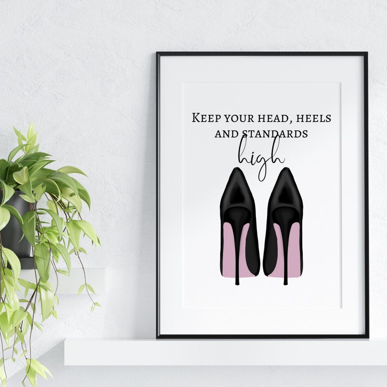 May include: A framed print featuring a pair of black high-heeled shoes with pink soles. The text "Keep your head, heels, and standards high" is displayed above the shoes in a stylish font. The artwork is set against a white background.