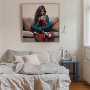 May include: A framed print shows a person sitting on a sofa, holding a white mug. The person wears teal clothing and white trainers. The sofa has floral cushions and a red patterned throw. The artwork hangs above a bed with grey and white bedding.