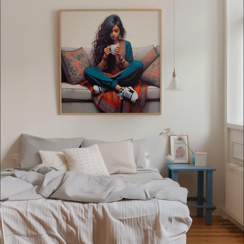 May include: A framed print shows a person sitting on a sofa, holding a white mug. The person wears teal clothing and white trainers. The sofa has floral cushions and a red patterned throw. The artwork hangs above a bed with grey and white bedding.