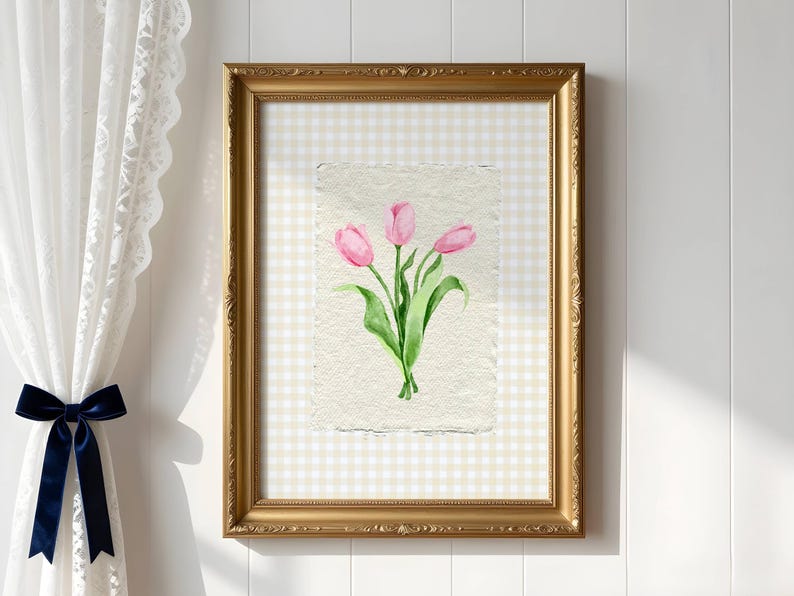 Pode incluir: Uma moldura dourada ornamentada retangular vertical contendo uma pintura em aquarela de tr&ecirc;s tulipas cor-de-rosa com caules e folhas verdes em papel texturizado branco sujo, sobre um fundo com padr&atilde;o xadrez vichy bege claro e branco.