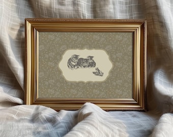 May include: A framed print with a gold-colored frame. The print features a sepia-toned illustration of kittens and a frog on a light beige background. The background has a floral pattern in a muted green color. The frame is rectangular.