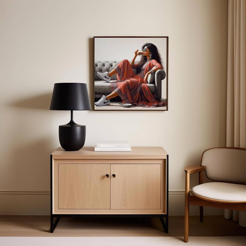 May include: A black table lamp with a lampshade, sitting on a light wood cabinet with black legs. A framed artwork depicts a person in a red dress and white sneakers. A wooden chair is next to the cabinet.