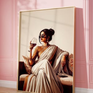 Puede incluir: Una obra de arte enmarcada representa a una mujer con un sari blanco, sosteniendo una copa de vino tinto. Lleva gafas de sol y joyas, sentada en un sof&aacute; con estampado floral. La obra tiene un marco dorado y est&aacute; sobre una pared rosa.