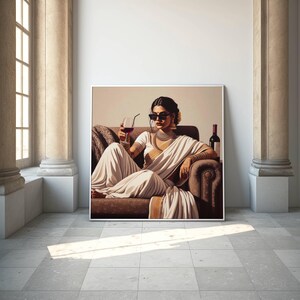 May include: A framed artwork depicts a person in a white sari, sunglasses, and jewelry, seated on a brown sofa, holding a glass of red wine. A wine bottle is visible. The artwork is displayed in a room with columns and a window.