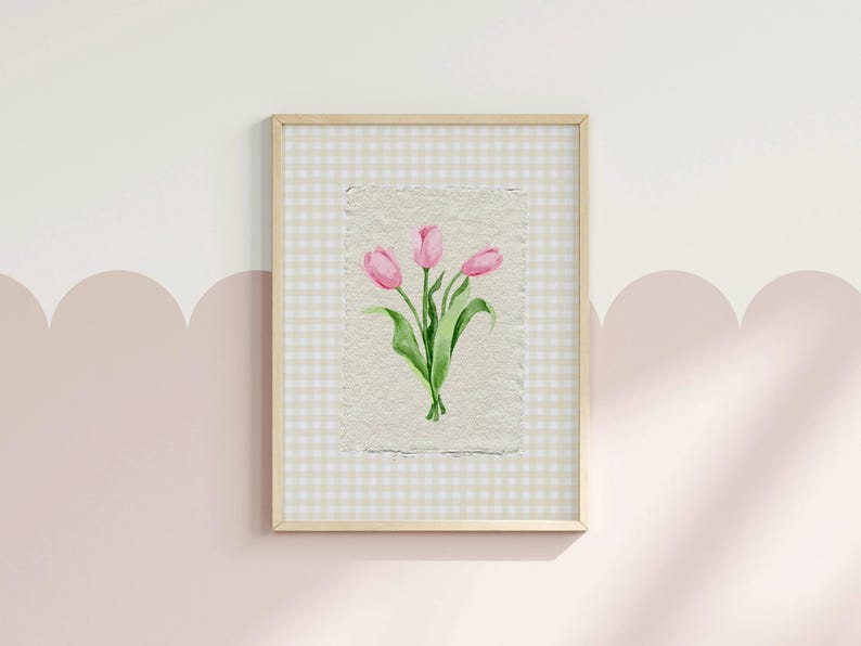 Pode incluir: Uma impress&atilde;o de arte emoldurada com uma aguarela de tr&ecirc;s t&uacute;lipas cor-de-rosa com caules e folhas verdes sobre papel texturado branco sujo. A obra de arte est&aacute; colocada sobre um fundo de xadrez vichy bege claro e branco numa moldura de madeira.