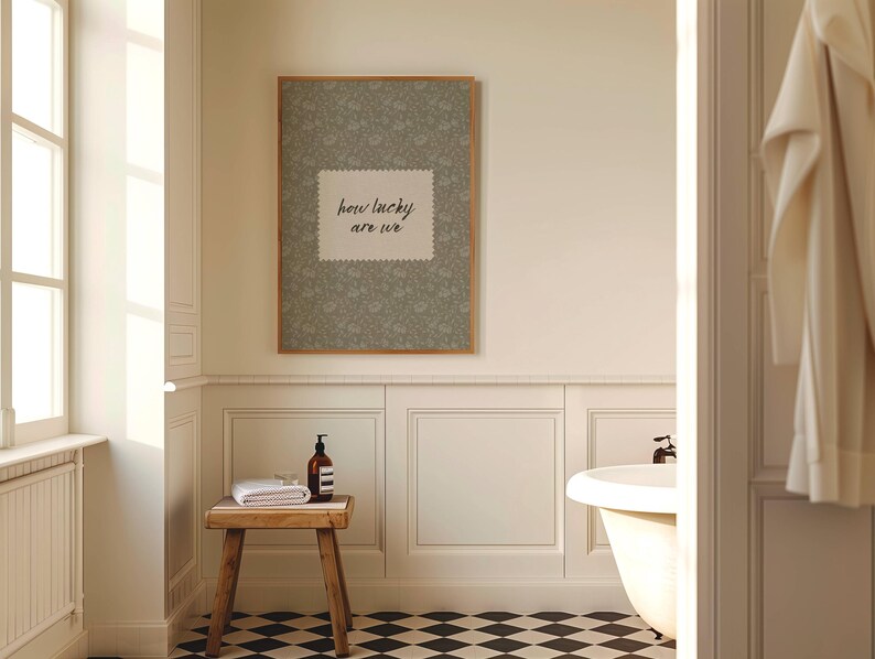 May include: A bathroom scene featuring a framed print with the text "how lucky are we" above a wooden stool. The stool holds a rolled white towel and a brown bottle. The room has a black and white checkered floor.