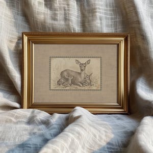May include: A framed print featuring a sepia-toned illustration of a doe with two fawns. The artwork is set within a gold-colored frame, adding a touch of elegance. The image is a vintage-style depiction of wildlife.