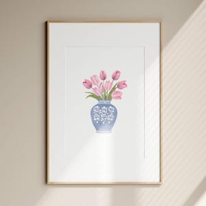 May include: A framed art print featuring a watercolor painting of pink tulips in a blue and white decorative vase. The vase has a floral design. The artwork is displayed in a white mat and a gold frame.