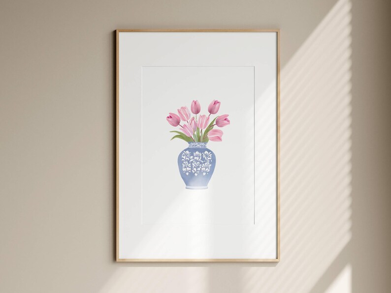 May include: A framed art print featuring a watercolor painting of pink tulips in a blue and white decorative vase. The vase has a floral design. The artwork is displayed in a white mat and a gold frame.