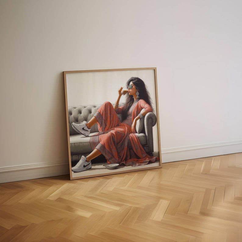 May include: A framed artwork depicts a person in a coral-colored outfit, seated on a gray tufted sofa, sipping from a cup. The person wears sunglasses and white sneakers. The artwork is leaning against a white wall on a wooden floor.