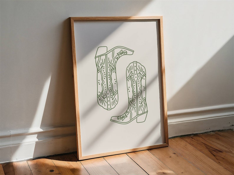 May include: A framed print showing a pair of green line-art cowboy boots. The boots have decorative stitching and are set against a neutral background. The artwork is displayed in a wooden frame.