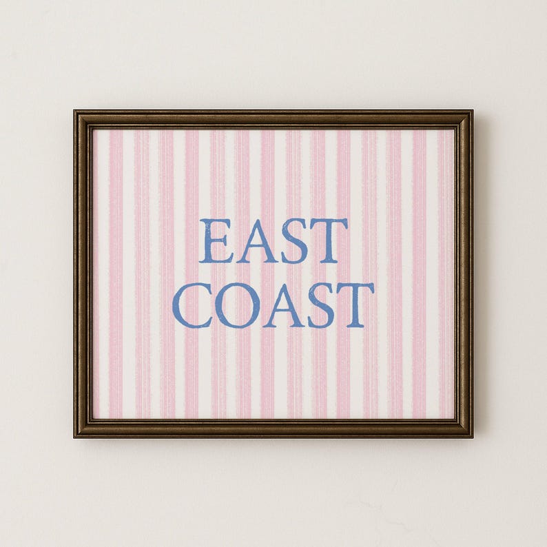 May include: Framed artwork with a brown border. The artwork features a pink and white striped background with the words "EAST COAST" in blue lettering. The artwork is rectangular and appears to be a print or poster.