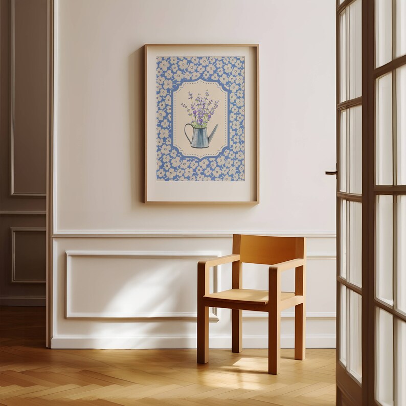 May include: A framed art print featuring a blue watering can filled with purple flowers. The artwork is set against a light blue background with a floral pattern and framed in a wooden frame. The print is displayed on a white wall.