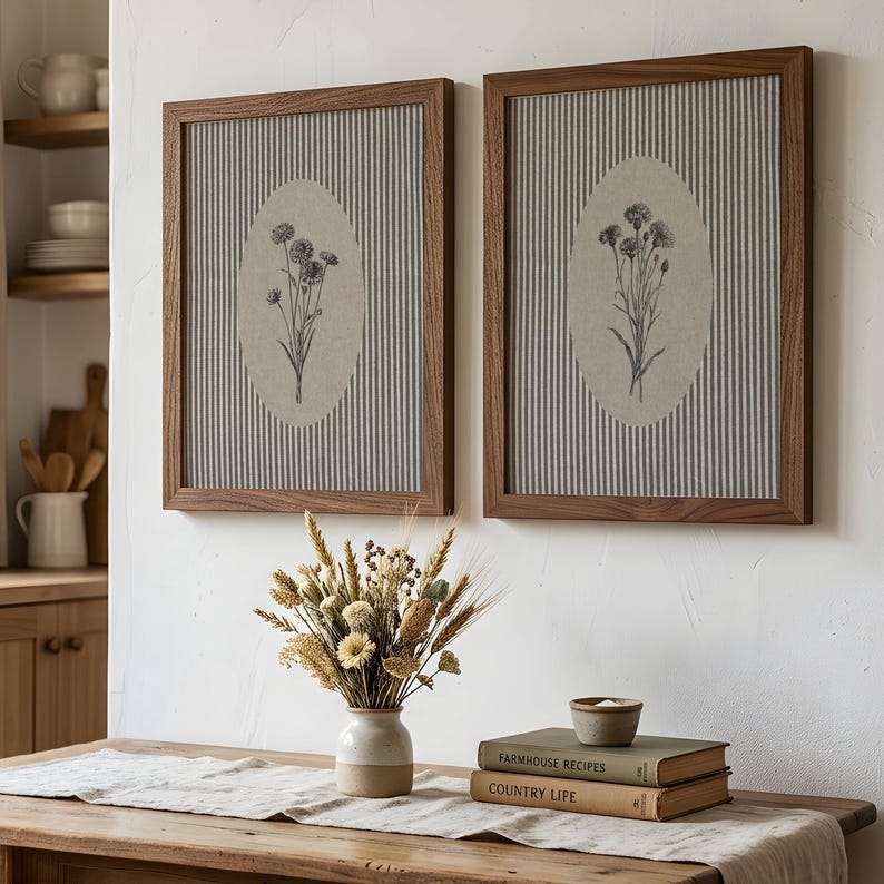 May include: Two rectangular wall art pieces with dark wood frames, featuring a gray and white vertical striped background and a central beige oval containing a detailed black and white botanical illustration of a cluster of wildflowers.