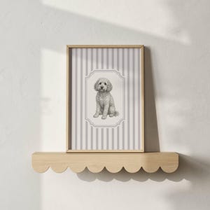 Puede incluir: Una impresión enmarcada con un boceto a lápiz de un perro blanco y esponjoso sentado. La obra de arte está sobre un fondo de rayas verticales grises y blancas, enmarcada en madera clara. La impresión descansa sobre una estantería de madera con volantes.