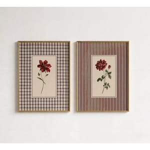 Pode incluir: Dois quadros retangulares com ilustrações botânicas. A impressão da esquerda mostra uma flor vermelha escura sobre um fundo bege com uma borda xadrez castanha e branca. A impressão da direita mostra uma rosa vermelha escura com folhas verdes sobre um fundo bege com uma borda de riscas verticais castanhas e brancas.