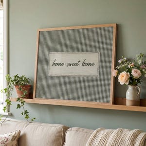 Peut inclure: Une décoration murale rectangulaire dans un cadre en bois clair avec un fond à motif vichy vert et blanc. Au centre, un empiècement en tissu aux bords effilochés affiche le texte en cursive noire home sweet home.