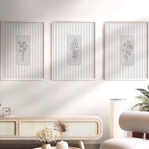 May include: Three framed botanical art prints. Each print displays a black and white floral illustration on a vertical striped backdrop. The white frames and minimalist design create an elegant aesthetic, ideal for home decor.