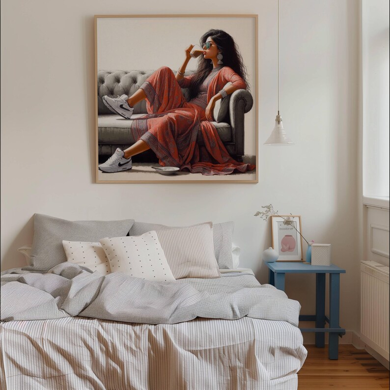 May include: A framed print depicts a person in a red outfit and sunglasses, seated on a gray sofa, sipping from a cup. The person wears white sneakers. The artwork hangs above a bed with gray and white striped bedding and pillows.
