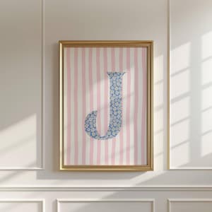 May include: Framed artwork featuring the letter "J" in a blue floral pattern. The background has pink and white vertical stripes. The gold frame adds a touch of elegance to this decorative piece, perfect for a nursery or bedroom.
