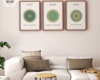 May include: Three framed prints with the words "MIND", "BODY", and "SOUL" above green and yellow gradient circles. The phrases "OPEN YOUR MIND", "NOURISH YOUR BODY", and "FEED YOUR SOUL" are below. A white sofa and cushions are in the foreground.