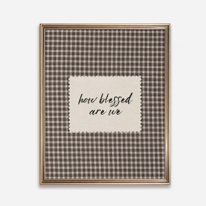 May include: Framed wall art featuring a brown and white checkered pattern background. A rectangular patch with a decorative edge in the center displays the handwritten text "how blessed are we" in black script. The frame is gold.