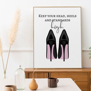 May include: Framed art print featuring a pair of black high heels with pink soles. The artwork includes the text "Keep your head, heels and standards high" in black lettering on a white background.