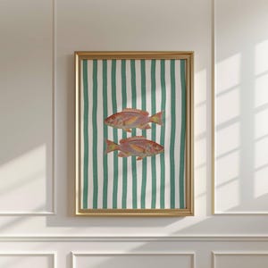 May include: Framed artwork featuring two orange and yellow fish on a green and white striped background. The artwork is in a gold frame and is displayed on a white wall. The fish are detailed and appear to be swimming.