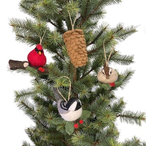 May include: Four felt Christmas ornaments hanging on a green artificial Christmas tree. The ornaments are a brown pine cone, a red cardinal, a gray chickadee, and a brown and white chipmunk.