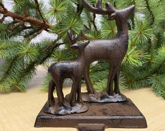 May include: A rustic brown cast iron stocking holder featuring a standing deer and a fawn. The holder has a distressed finish and is perfect for hanging stockings on a fireplace mantel.