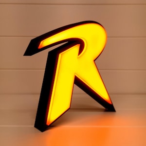 May include: A black and yellow 3D printed letter R, illuminated from within, resembling the Robin logo from the Batman comics.