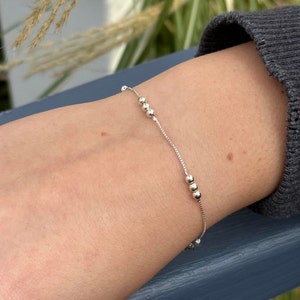 May include: A silver chain bracelet with small round beads. The bracelet is on a person's wrist.