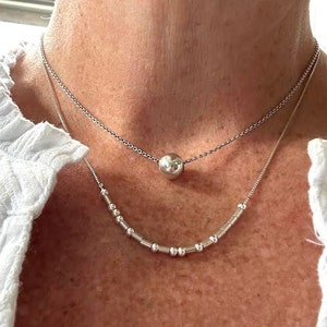 May include: Two silver necklaces, one with a large round pendant and the other with a row of small round beads.