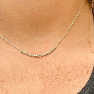 May include: A silver chain necklace with a row of small silver beads in the center.