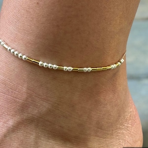 May include: A delicate silver and gold beaded anklet. The anklet is made with small, round silver beads and gold spacer beads.