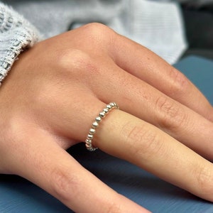 May include: A silver beaded ring on a finger with red nail polish.