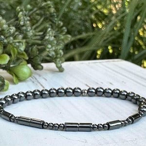 May include: A black hematite beaded bracelet with silver accents. The bracelet is made of small round beads and larger rectangular beads.