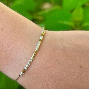 May include: A delicate bracelet with alternating gold and silver beads. The bracelet is on a person's wrist.