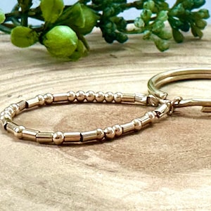 Peut inclure: Un bracelet doré avec de petites perles rondes et de plus grandes perles rectangulaires. Le bracelet est relié à un anneau doré plus grand.