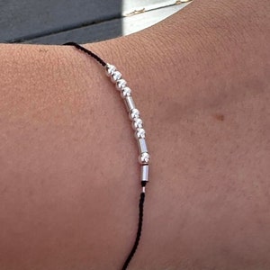 May include: A simple black string bracelet with silver beads and spacers.