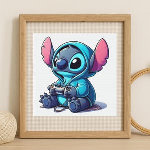 May include: Framed print of a cartoon character in a blue hoodie, holding a video game controller. The character has large ears and big eyes. The artwork is set against a white background with a cross-stitch texture, framed in light wood.