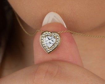May include: A gold heart-shaped pendant necklace with a clear cubic zirconia stone in the center. The pendant is surrounded by smaller cubic zirconia stones.