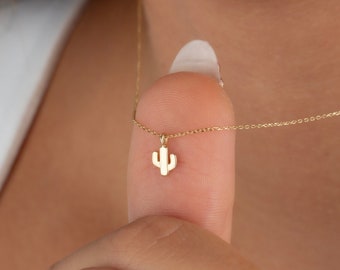 May include: A gold chain necklace with a small, delicate cactus pendant. The pendant is made of gold and has a simple, minimalist design.