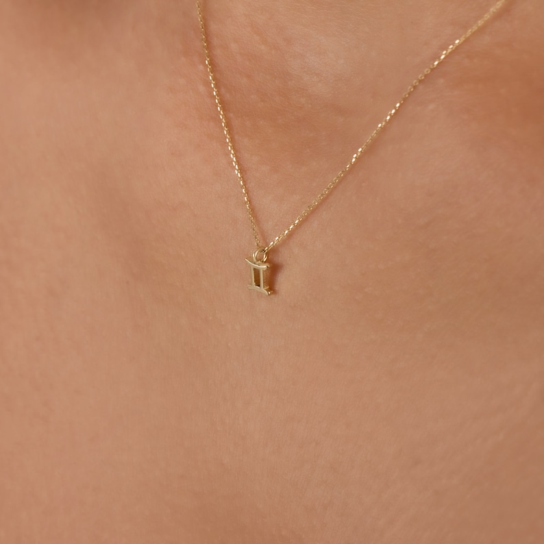 May include: A gold chain necklace with a small gold Gemini zodiac sign pendant.
