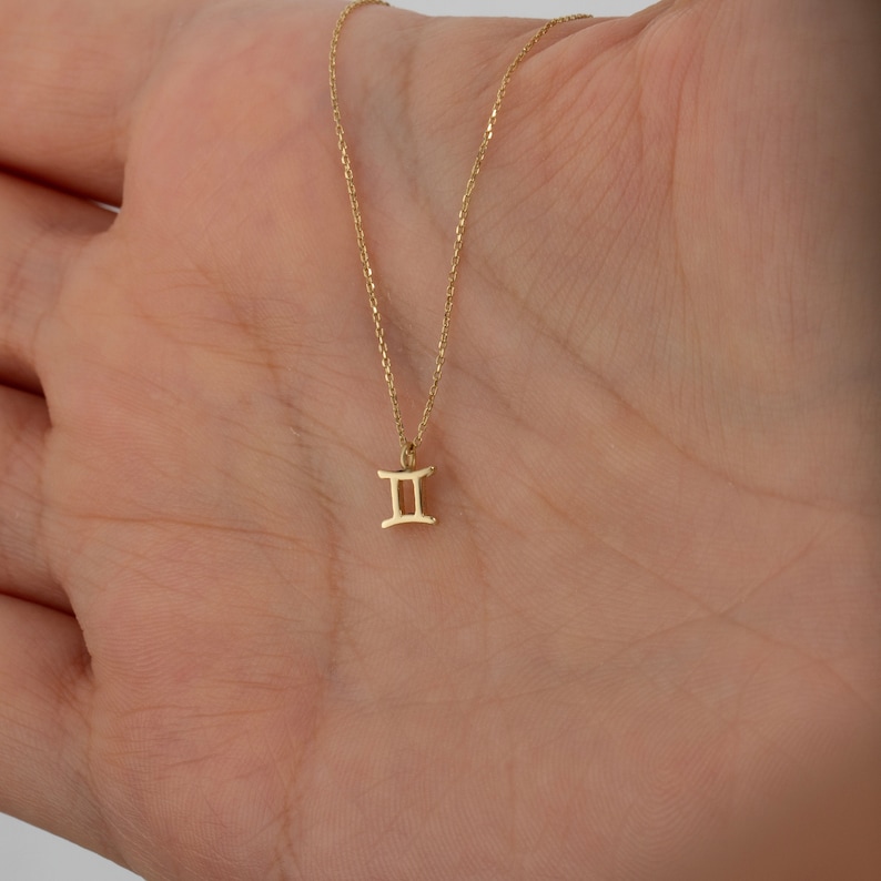 May include: A gold chain necklace with a small Gemini zodiac symbol pendant.