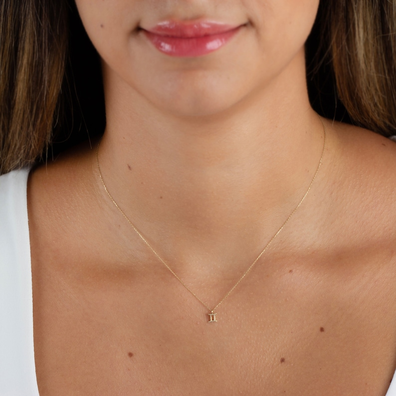 May include: A delicate gold chain necklace with a small Gemini zodiac symbol pendant.